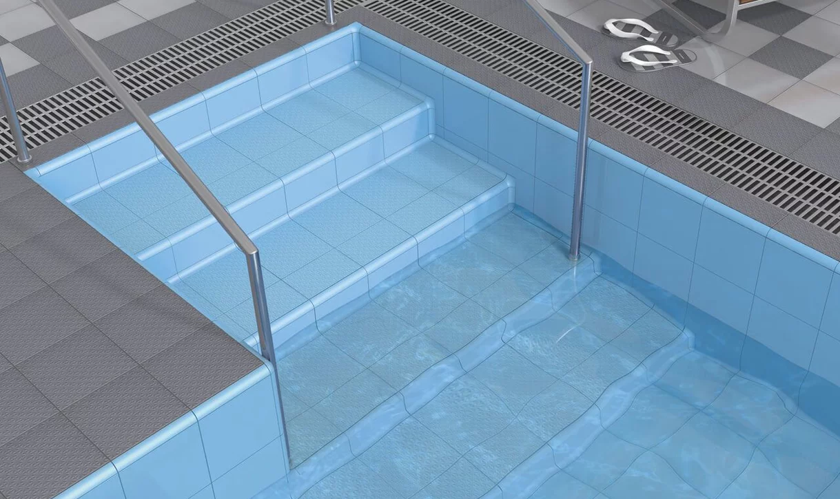 Nowoczesny basen wewnętrzny z jasnoniebieskimi płytkami ceramicznymi i szarymi antypoślizgowymi płytkami na podłodze.