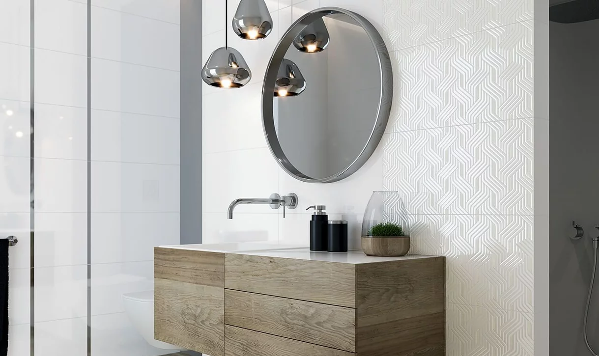 Nowoczesna łazienka z białymi błyszczącymi i geometrycznymi płytkami oraz drewnopodobną szafką i okrągłym lustrem.