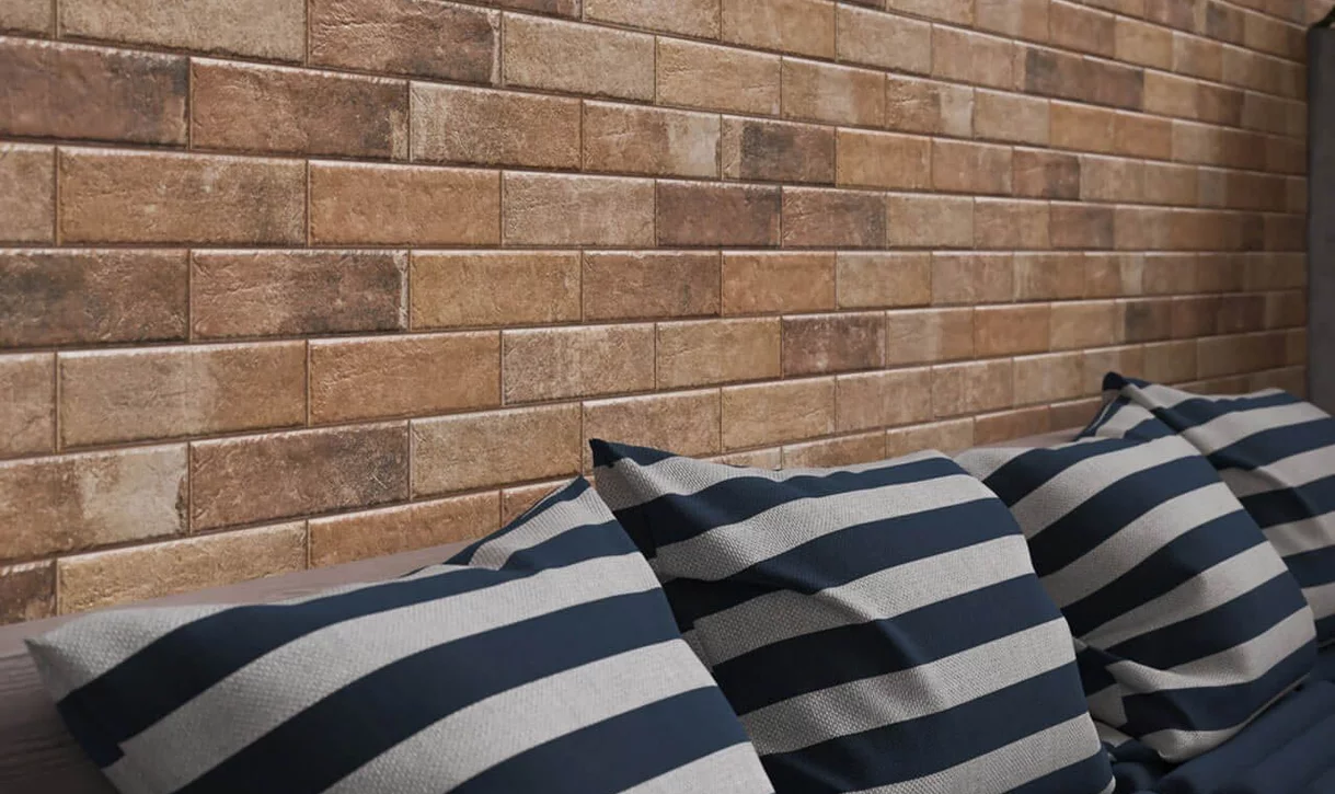 Zbliżenie na ścianę z prostokątnymi płytkami kamieniopodobnymi w ciepłych odcieniach i poduszki w paski.