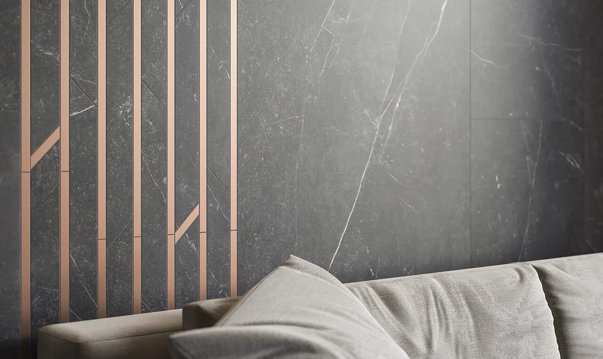 Nowoczesna ściana z ciemnymi płytkami marmurowymi z białym żyłkowaniem i metalicznymi paskami oraz jasnoszara sofa.