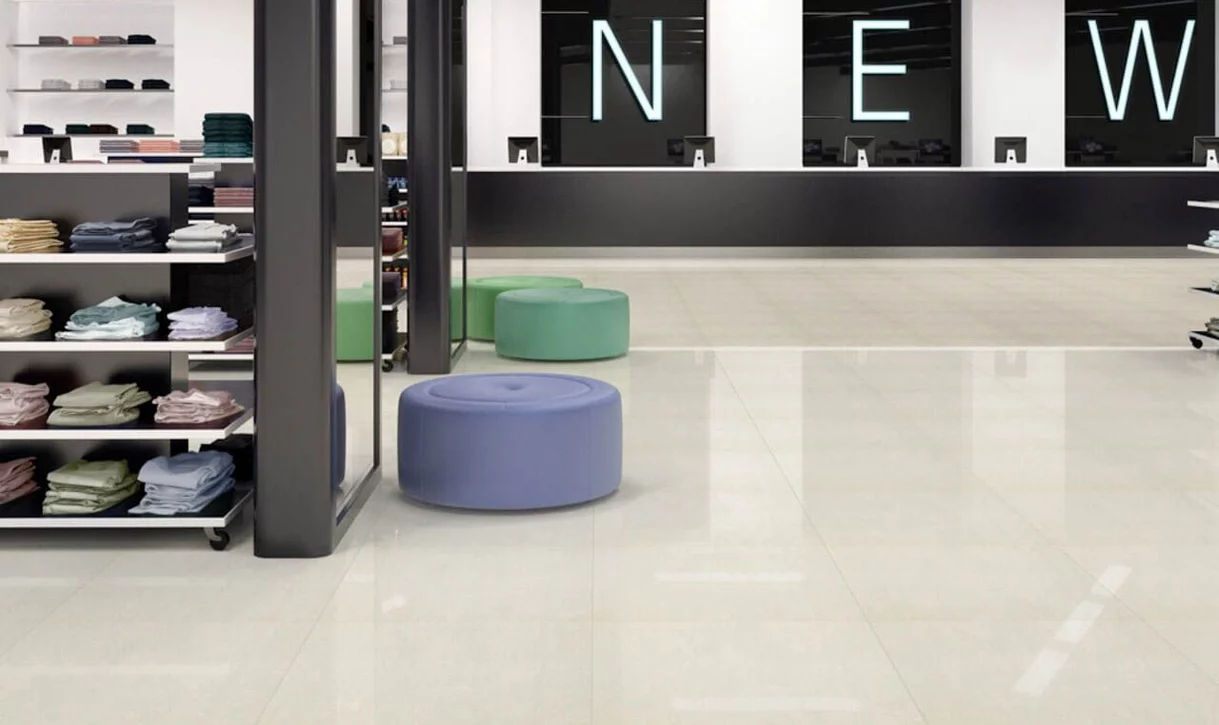 Nowoczesne wnętrze sklepu z dużymi błyszczącymi jasnymi płytkami porcelanowymi na podłodze i pastelowymi pufami.