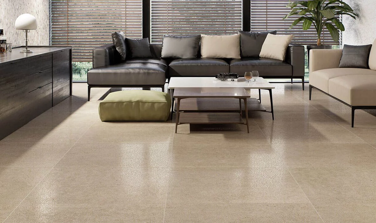 Nowoczesny salon z dużymi matowymi płytkami kamieniopodobnymi w ciepłym beżu i ciemną sofą.