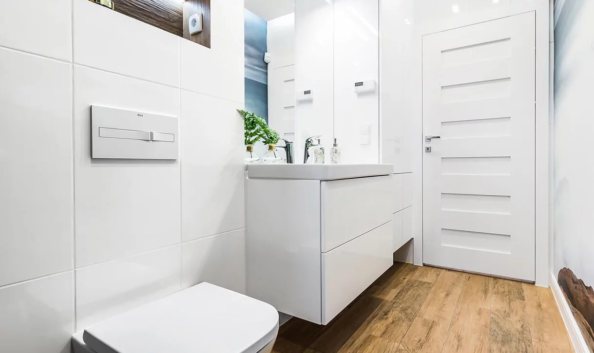 Nowoczesna łazienka z dużymi białymi ceramicznymi płytkami na ścianach i drewnopodobną podłogą.