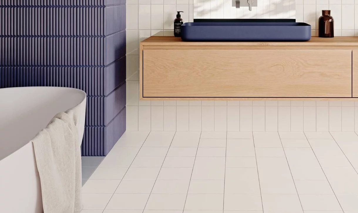 Łazienka w stylu skandynawskim z jasnymi kwadratowymi płytkami ceramicznymi i granatowym akcentem oraz drewnianą umywalką.