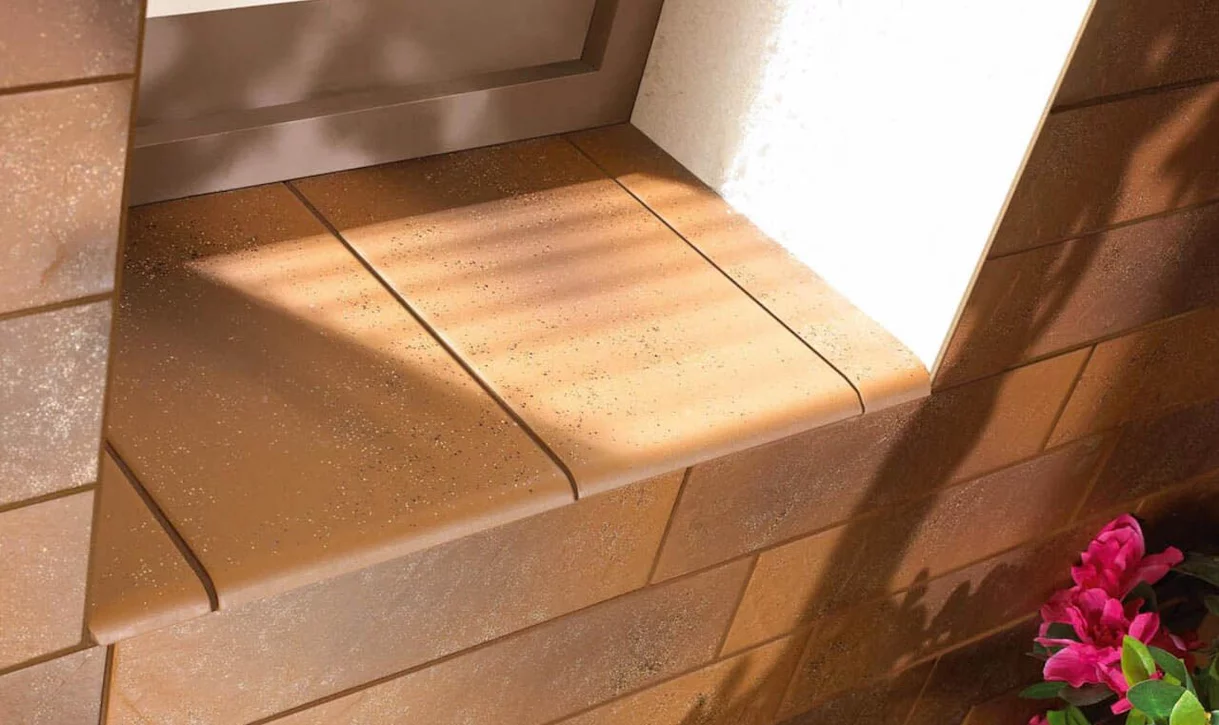 Zbliżenie na parapet z terakotowymi płytkami elewacyjnymi i różowymi kwiatami.