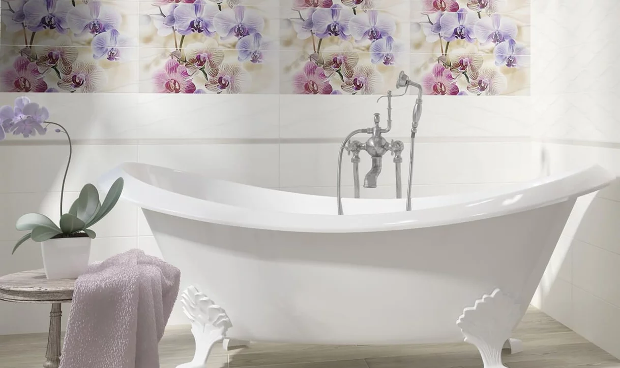 Elegancka łazienka z białymi ceramicznymi płytkami i dekoracyjnym pasem kwiatowym oraz wanną na nóżkach.