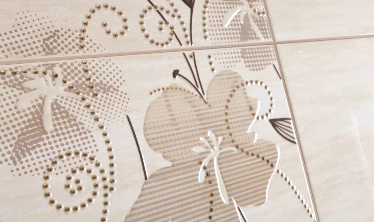 Zbliżenie na dekoracyjne ceramiczne płytki ścienne w jasnobeżowym kolorze z kwiatowym wzorem i złotymi akcentami.