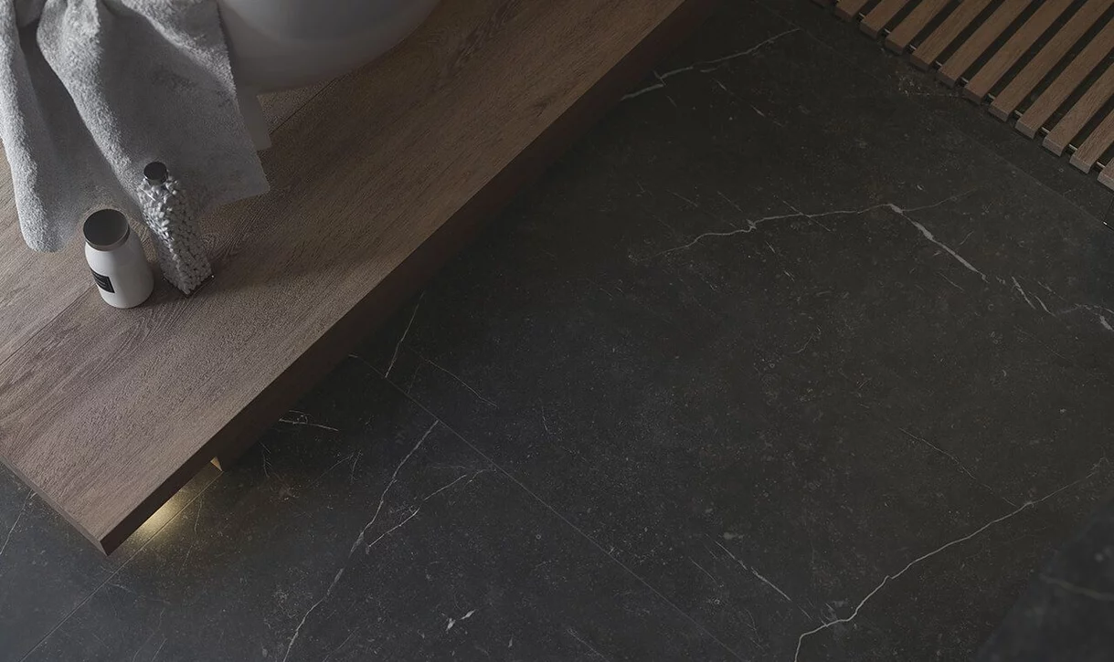 Nowoczesny kąt łazienki z ciemnymi płytkami marmurowymi na podłodze i drewnianą ławką.