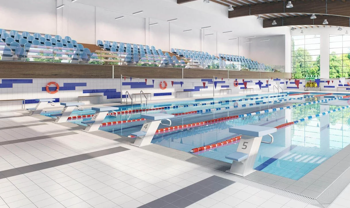 Jasny basen kryty z jasnymi ceramicznymi płytkami na podłodze i białymi płytkami ściennymi z niebieskimi akcentami.