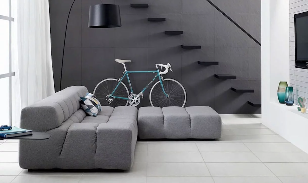 Nowoczesny salon z jasnoszarymi płytkami imitującymi beton na podłodze i ciemnymi teksturowanymi płytkami na ścianie.