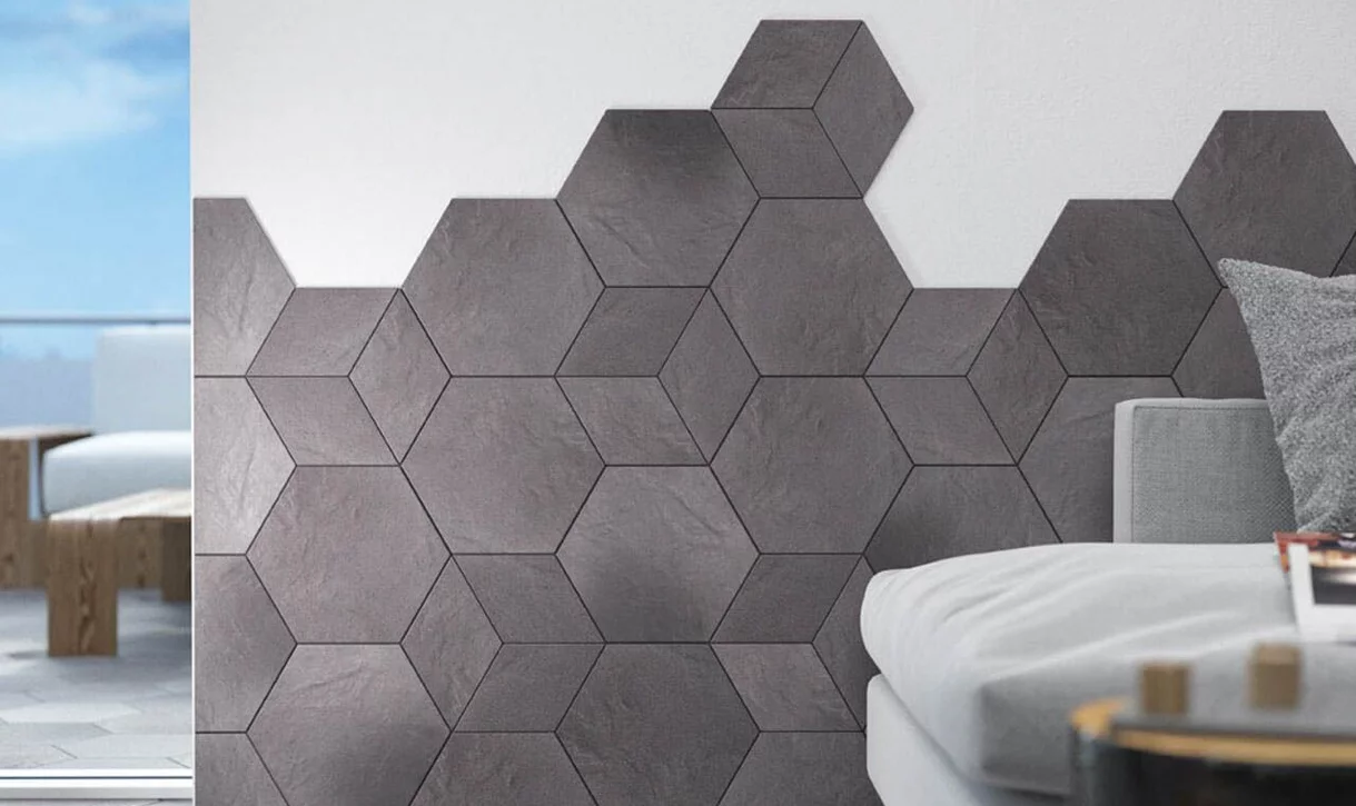 Zbliżenie na narożnik z ciemnoszarymi sześciokątnymi płytkami kamieniopodobnymi na białej ścianie i szarą sofą.
