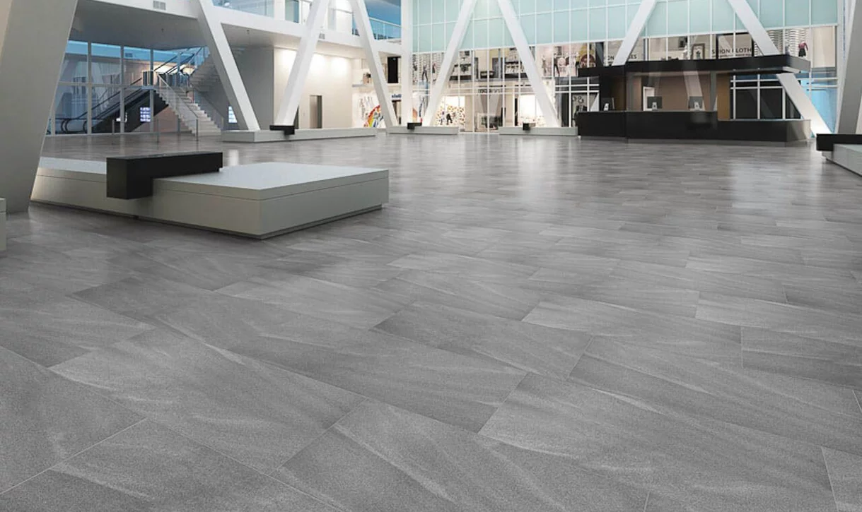 Przestronne wnętrze w stylu industrialnym z szarymi płytkami kamieniopodobnymi na podłodze i czarno-białymi meblami.