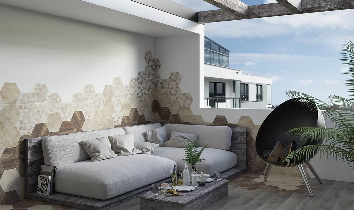 Stylowy taras z heksagonalnymi płytkami kamieniopodobnymi i drewnopodobnymi oraz szarą sofą i zielenią.
