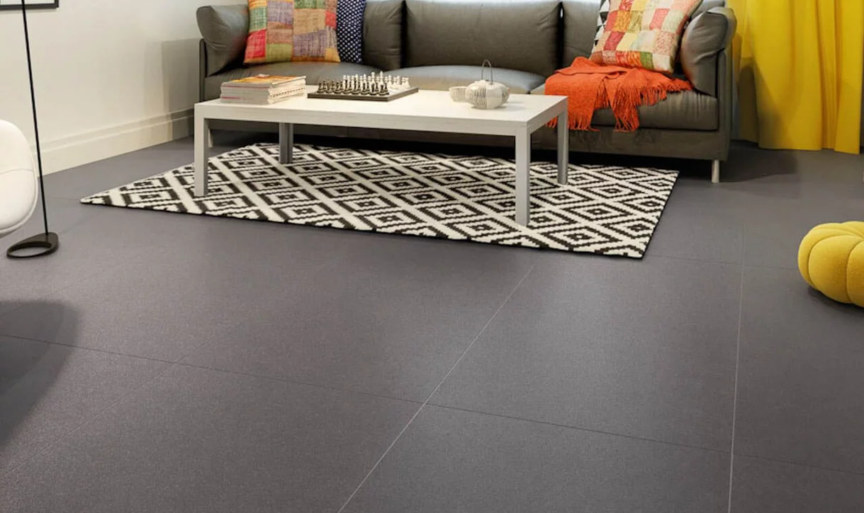 Nowoczesny salon z matowymi szarymi płytkami imitującymi beton na podłodze i kolorowymi tekstyliami.