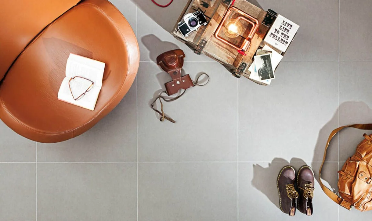 Przytulny kąt wnętrza z matowymi szarymi płytkami imitującymi beton i karmelowym skórzanym fotelem.