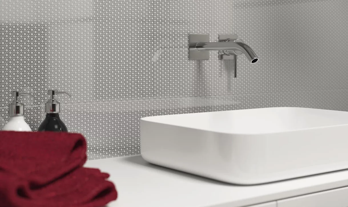 Zbliżenie na białą umywalkę prostokątną z szarą ścianą z małych sześciokątnych płytek.