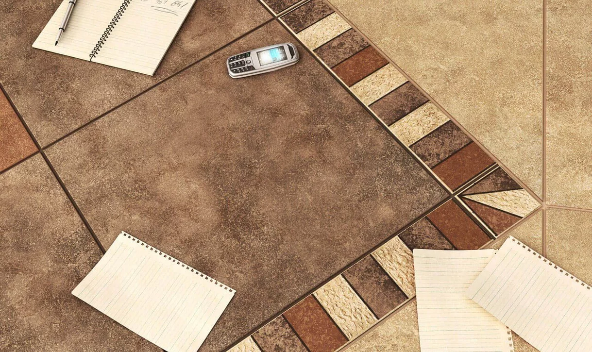 Zbliżenie na podłogę z rustykalnymi płytkami kamieniopodobnymi w ciepłych odcieniach z dekoracyjną bordiurą i starym telefonem.