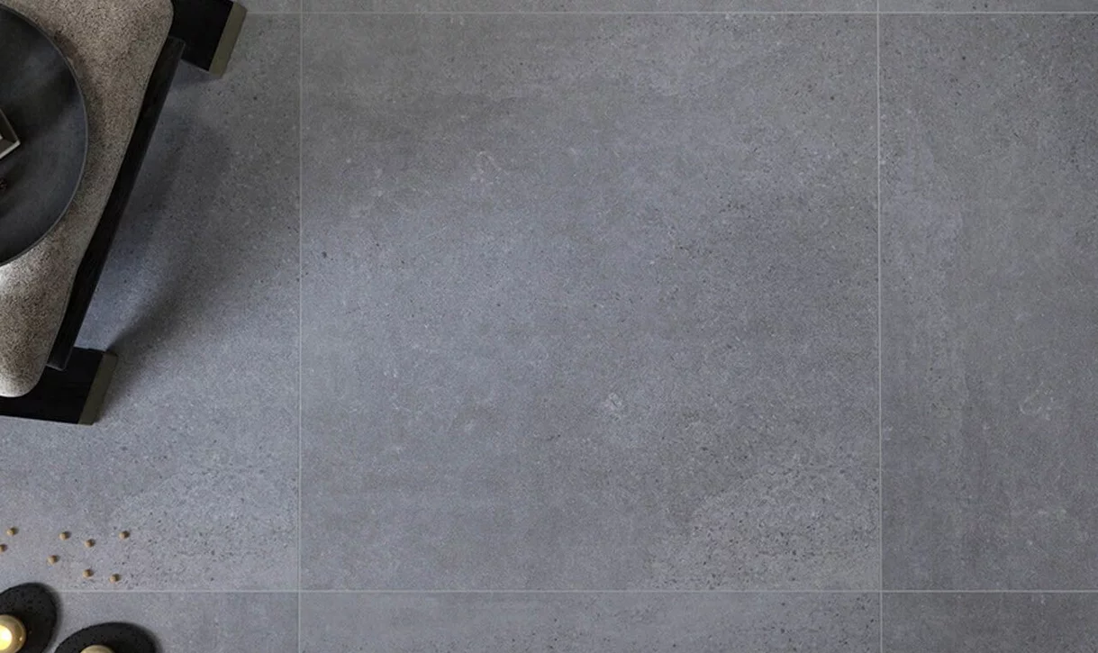 Minimalistyczny kąt wnętrza z dużymi szarymi płytkami imitującymi beton i meblami tapicerowanymi.