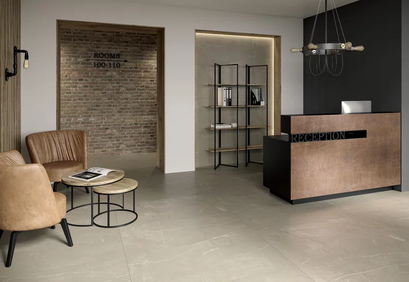 Recepcja z dużymi beżowymi płytkami marmurowymi z kolekcji Linearstone oraz brązową ladą i skórzanymi krzesłami.