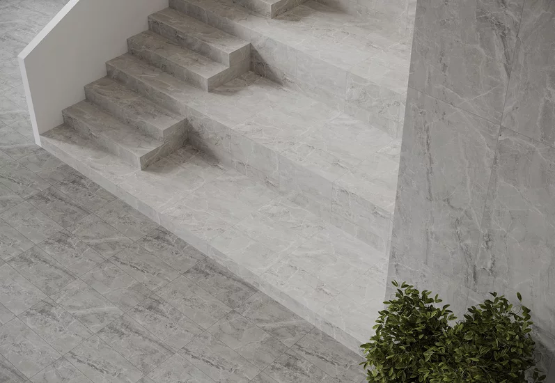 Nowoczesne wnętrze ze schodami i szarymi płytkami inspirowanymi kamieniem z kolekcji Little Rocks oraz zieloną rośliną.