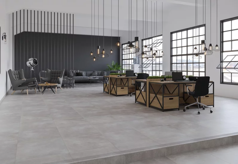 Industrialne biuro z jasnoszarymi płytkami imitującymi beton z kolekcji Magnetik oraz ciemnoszarymi meblami i drewnianymi biurkami.