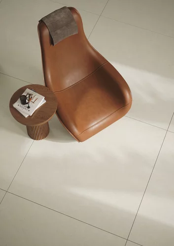 Minimalistyczne wnętrze z jasnobeżowymi płytkami inspirowanymi kamieniem z kolekcji Mild Desert oraz skórzanym fotelem i drewnianym stolikiem.