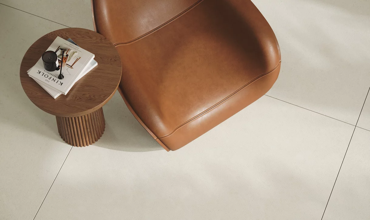 Nowoczesny kącik do czytania z beżowymi płytkami Mild Desert, skórzanym fotelem i okrągłym stolikiem.