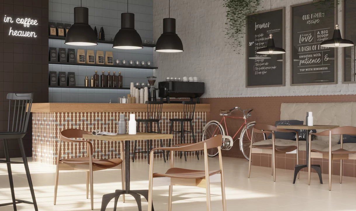 Przytulna kawiarnia z jasnobeżowymi i mozaikowymi płytkami z kolekcji Modernizm oraz drewnianymi meblami i czarnymi lampami.