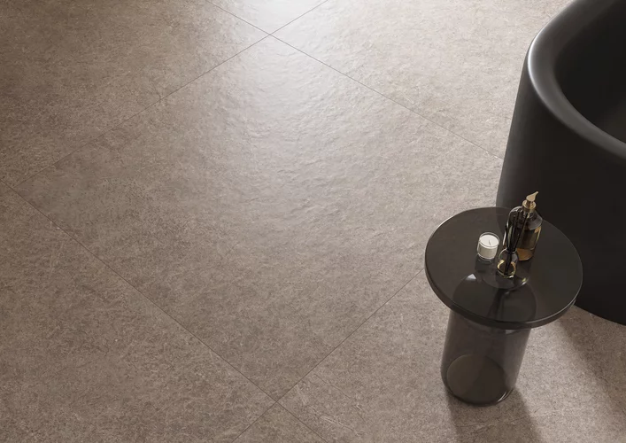 Szarobrązowe płytki Urban Champagne z kontrastującą czarną wanną i okrągłym, designerskim stolikiem.