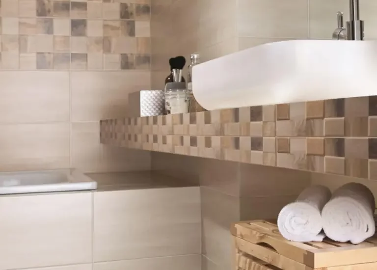 Łazienka z dużymi gładkimi beżowymi płytkami i dekoracyjnym pasem mozaiki wokół umywalki.