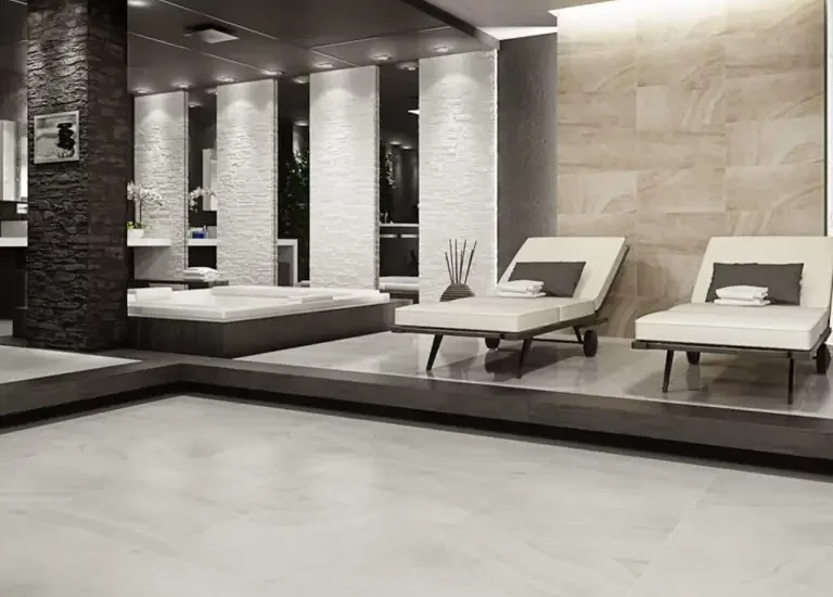 Nowoczesna strefa spa z jasnymi płytkami kamieniopodobnymi na podłodze i ścianach oraz białymi leżakami.