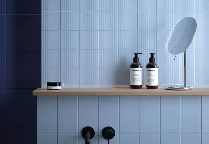 Minimalistyczna ściana łazienki z błękitnymi płytkami ceramicznymi i drewnianą półką.