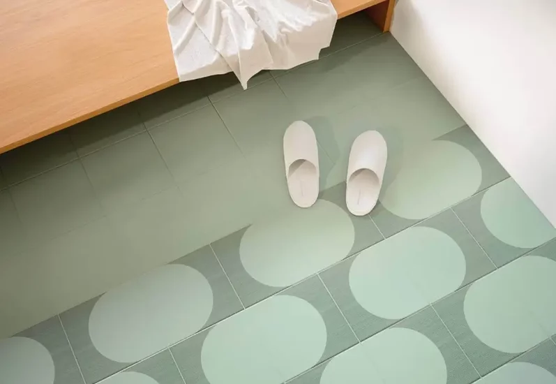 Minimalistyczne wnętrze z dużymi ceramicznymi płytkami podłogowymi o geometrycznym wzorze i drewnianą ławką z kapciami.