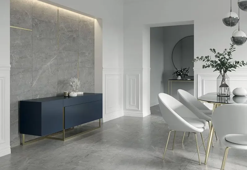 Nowoczesna jadalnia z dużymi szarymi płytkami marmurowymi na podłodze i ścianie oraz białymi krzesłami z złotymi nogami.