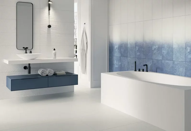 Nowoczesna łazienka z białymi i niebieskimi kamieniopodobnymi płytkami oraz niebieską wiszącą szafką i białą wanną.