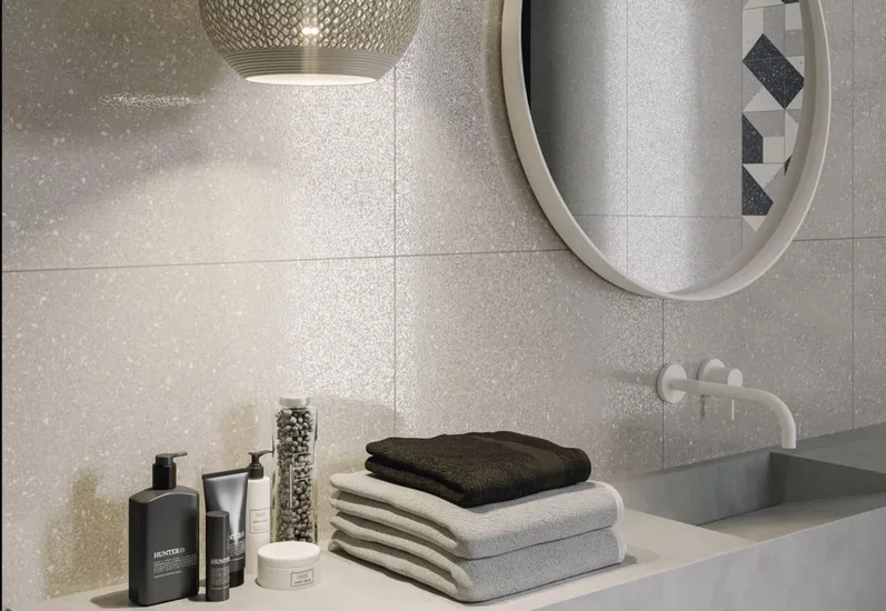 Minimalistyczna łazienka z jasnoszarymi błyszczącymi płytkami ceramicznymi na ścianach i nowoczesną umywalką.