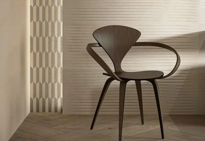 Minimalistyczne wnętrze z beżowymi płytkami ściennymi o fakturze i geometrycznymi płytkami kamieniopodobnymi oraz drewnopodobną podłogą.