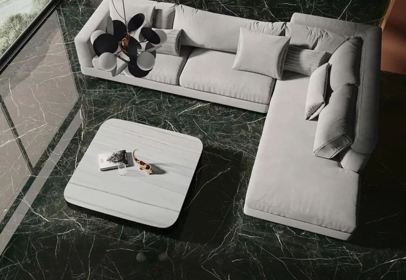 Nowoczesny salon z dużymi ciemnozielonymi płytkami marmurowymi na podłodze i jasnoszarą sofą.