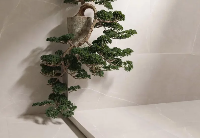 Minimalistyczne wnętrze z jasnobeżowymi płytkami marmurowymi na ścianach i podłodze oraz rośliną w kamiennym doniczce.