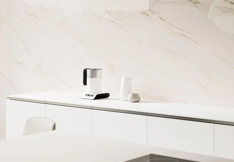 Minimalistyczna kuchnia z białymi meblami i marmurowym panelem na ścianie.